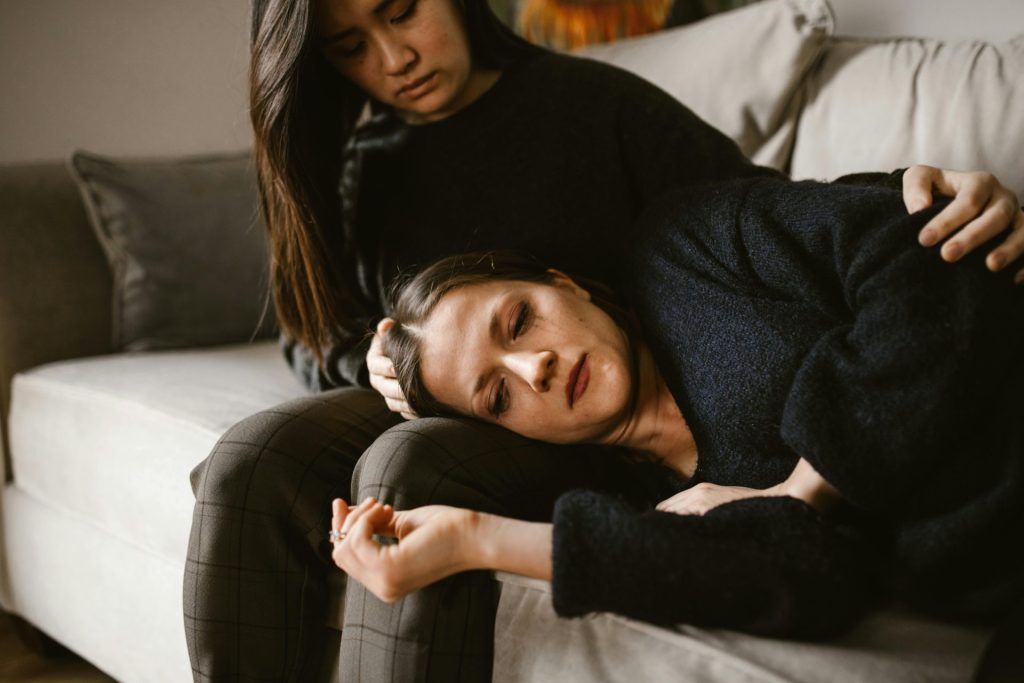 Two women on a couch, one comforting the other, depicting empathy and support.